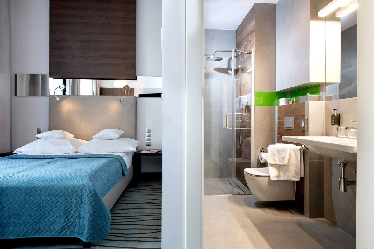Une chambre d’hôtel moderne équipée d’un lit, d’une table de chevet et d’une salle de bain avec douche, toilettes et lavabo.