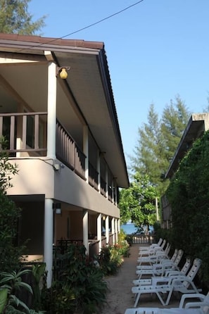 A hotel with a covered outdoor seating area, a second floor balcony, and a view of the sea.