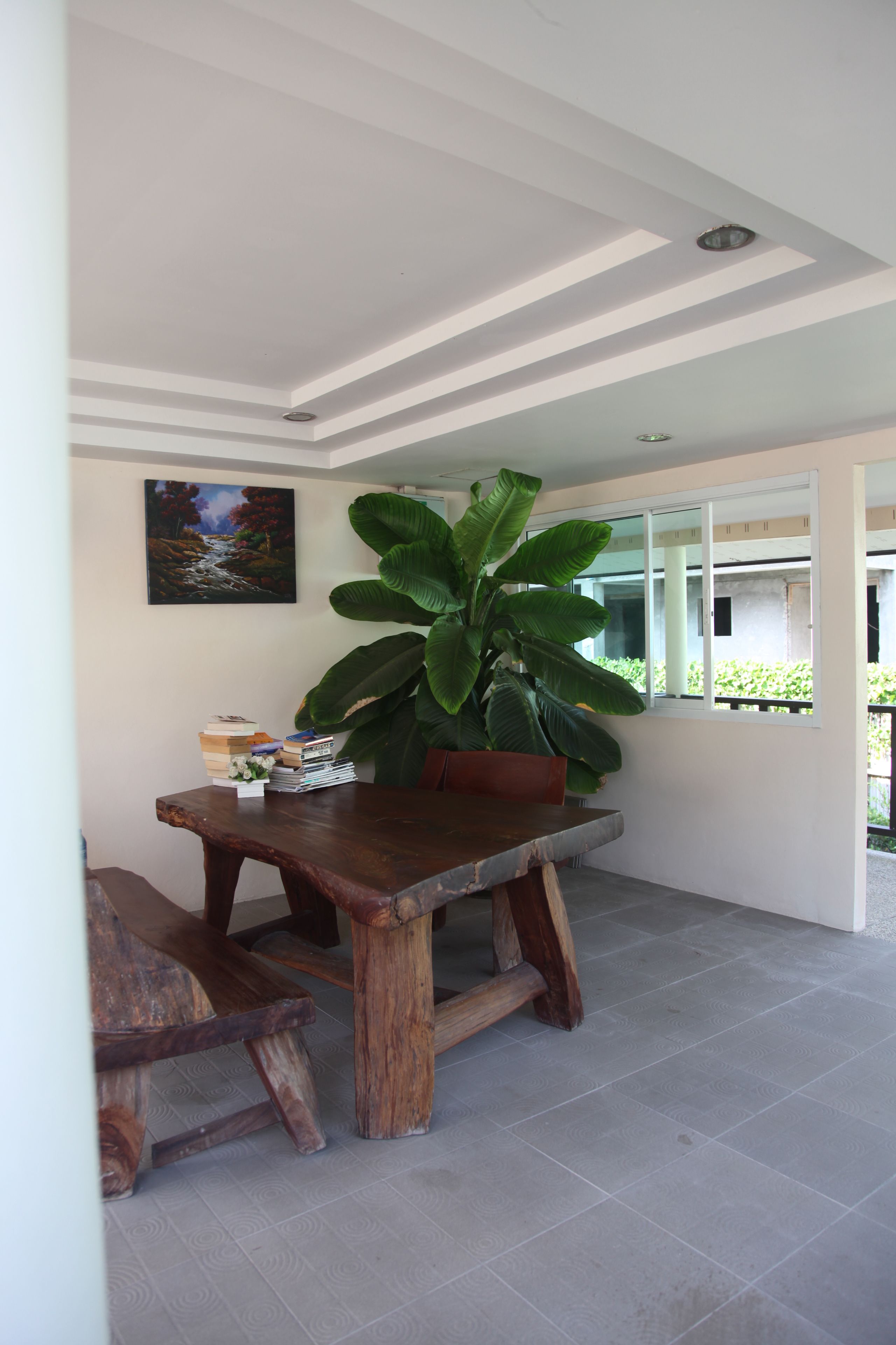 A dining area with a wooden table, a large potted plant, and a painting on the wall.