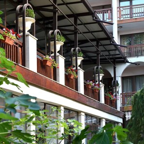 Un edificio de varios pisos con balcones, grandes ventanales y macetas colgantes con flores.