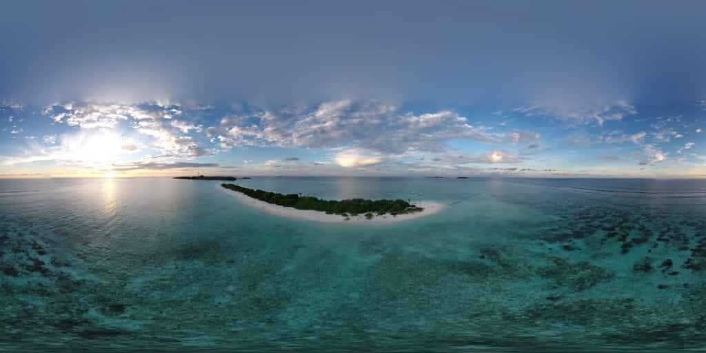 A panoramic view of a tropical island with clear turquoise waters and a small island with lush greenery in the center.