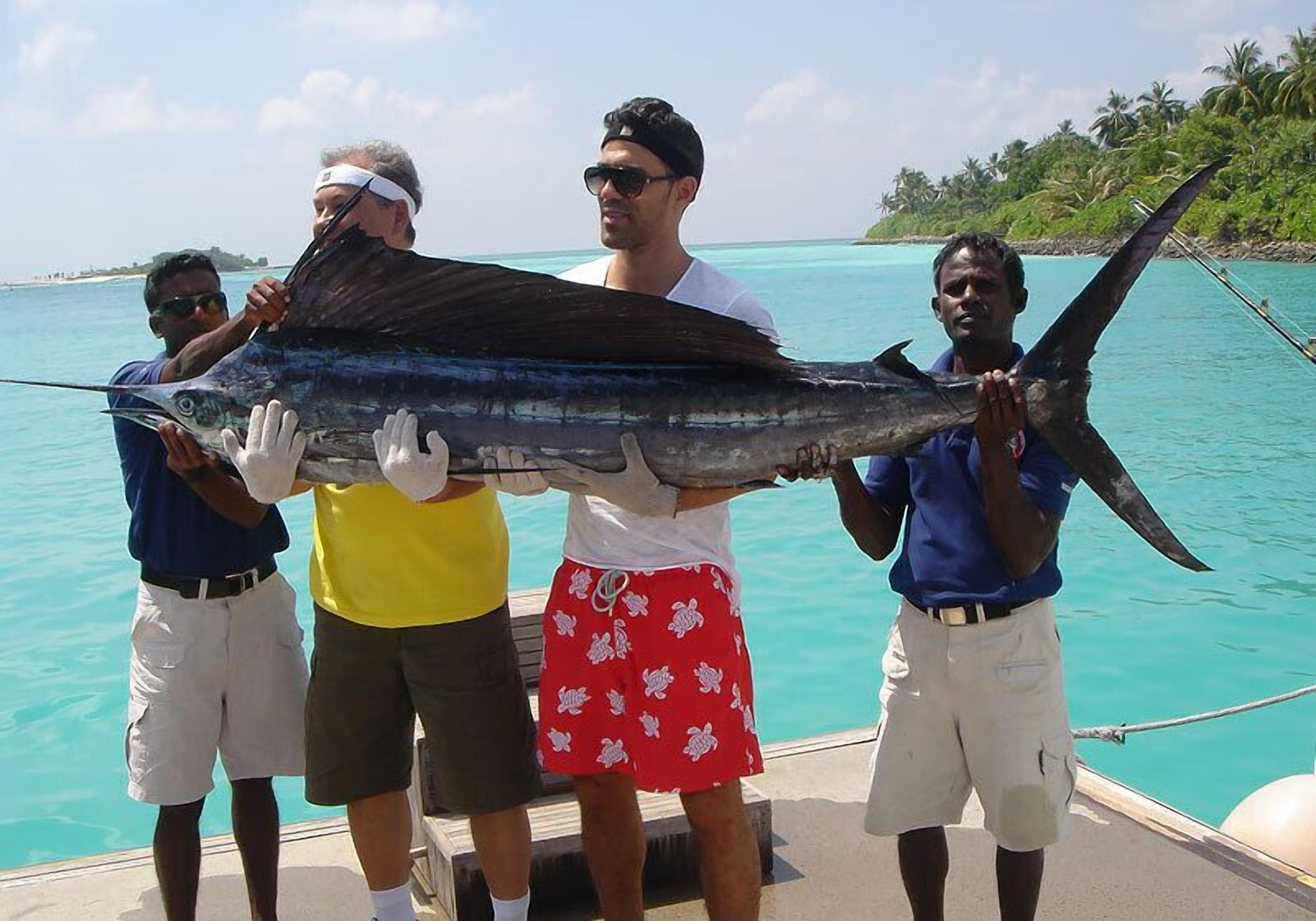 Um grupo de pessoas segurando um peixe grande em um barco, com vista clara para o oceano e uma ilha distante.