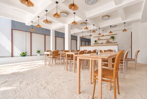 Quarto amplo com uma longa mesa de madeira e cadeiras, várias luminárias pendentes e uma grande janela que proporciona luz natural.