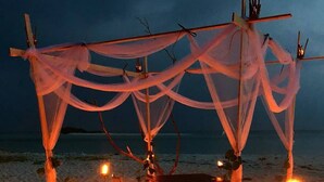 A beach setting with a canopy structure, a table, chairs, and candles.