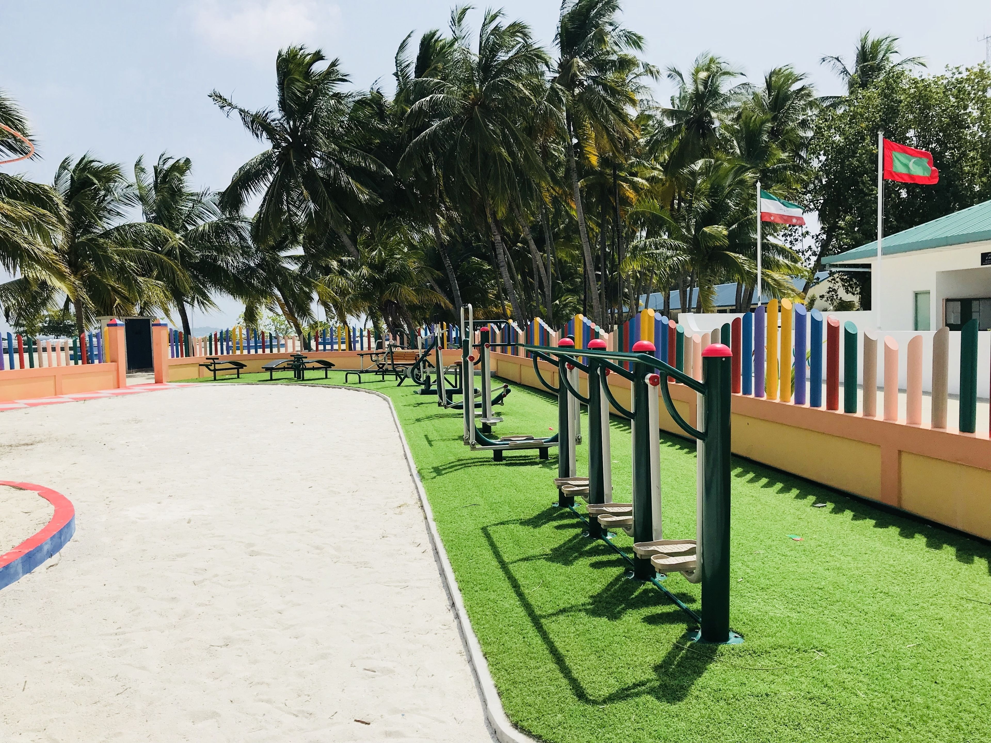 Un parque infantil con equipo de ejercicios, zona de arena y palmeras.