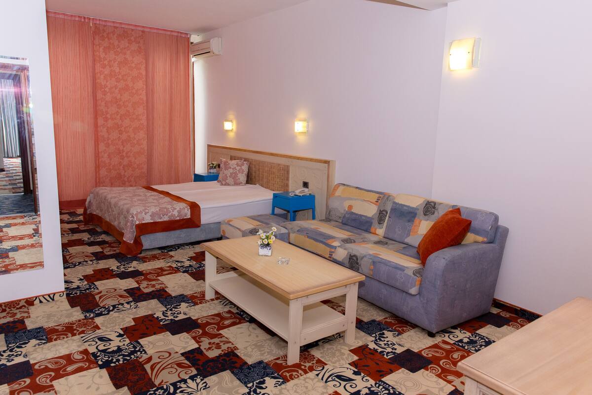 A hotel room with a bed, a sofa, a small table, and a patterned carpet.