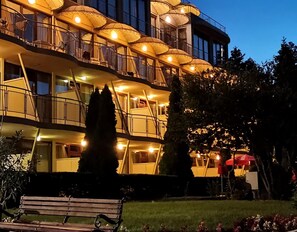 A multi-story hotel with balconies, outdoor lighting, and a bench in the foreground. - Hotel Koral (Varna)