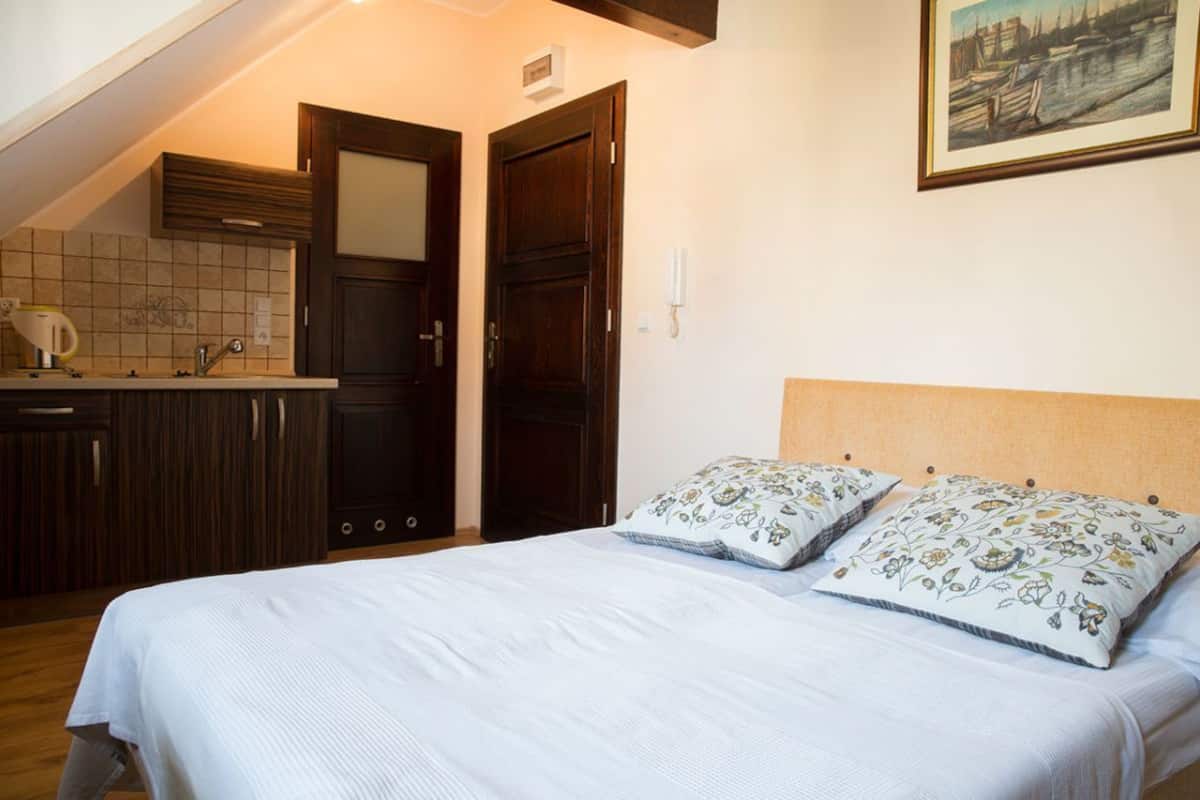A bedroom with a bed, two pillows, a nightstand, a window, and a door.