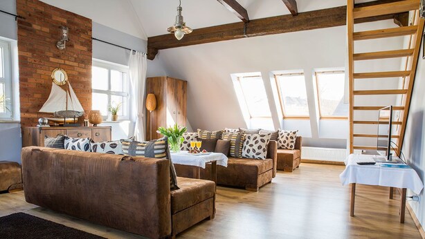 Una sala de estar acogedora con pisos de madera, sofás marrones y una pared de ladrillo.