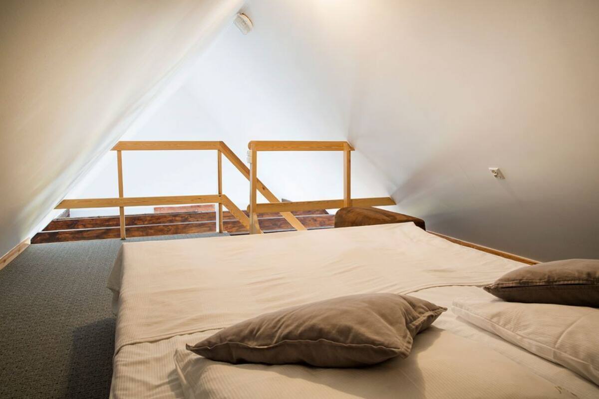 A small, cozy attic bedroom with a sloped ceiling, a wooden ladder, and a single bed with pillows.