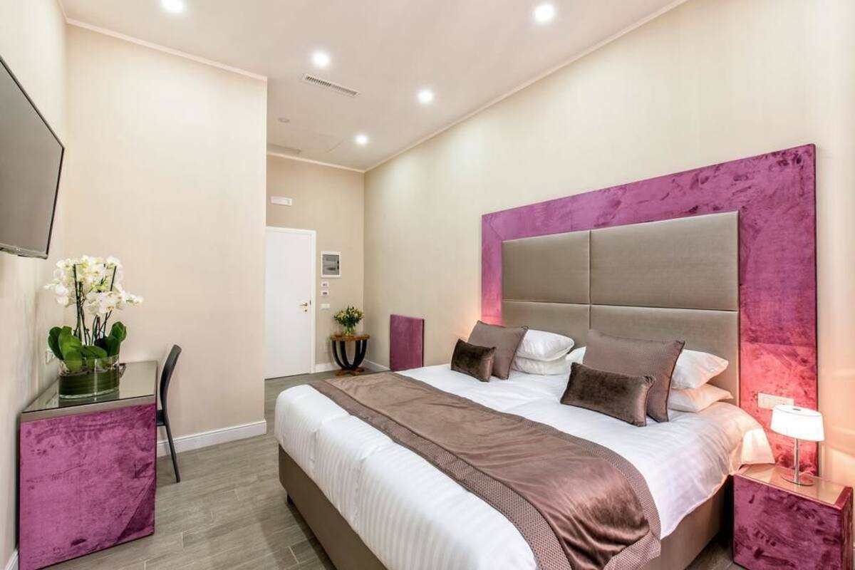 A modern bedroom with a large bed, a bedside table, a TV, and a desk with a chair.