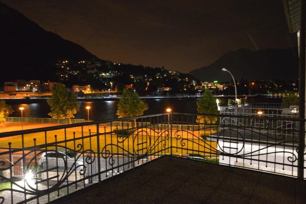 A nighttime view of a riverside area with a metal railing, a bridge, and buildings in the background.