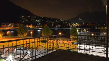 A nighttime view of a riverside area with a metal railing, a bridge, and buildings in the background.