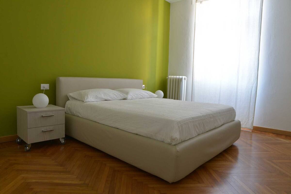 A bedroom with a bed, a nightstand, a bedside table, and a radiator.
