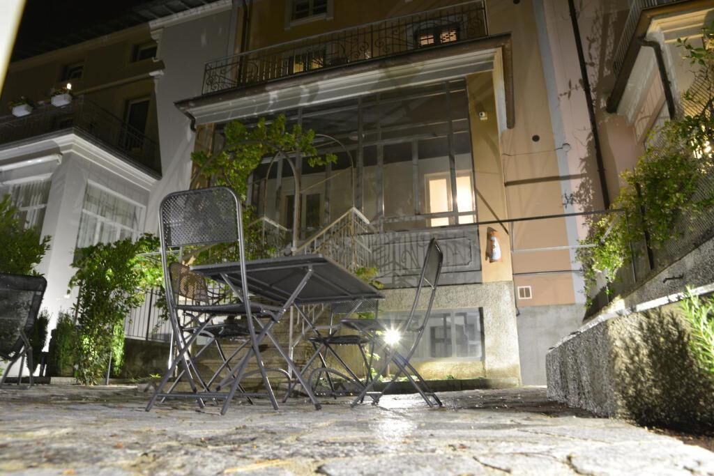 A street view at night with a metal chair and table in the foreground, a building with balconies and windows in the background.