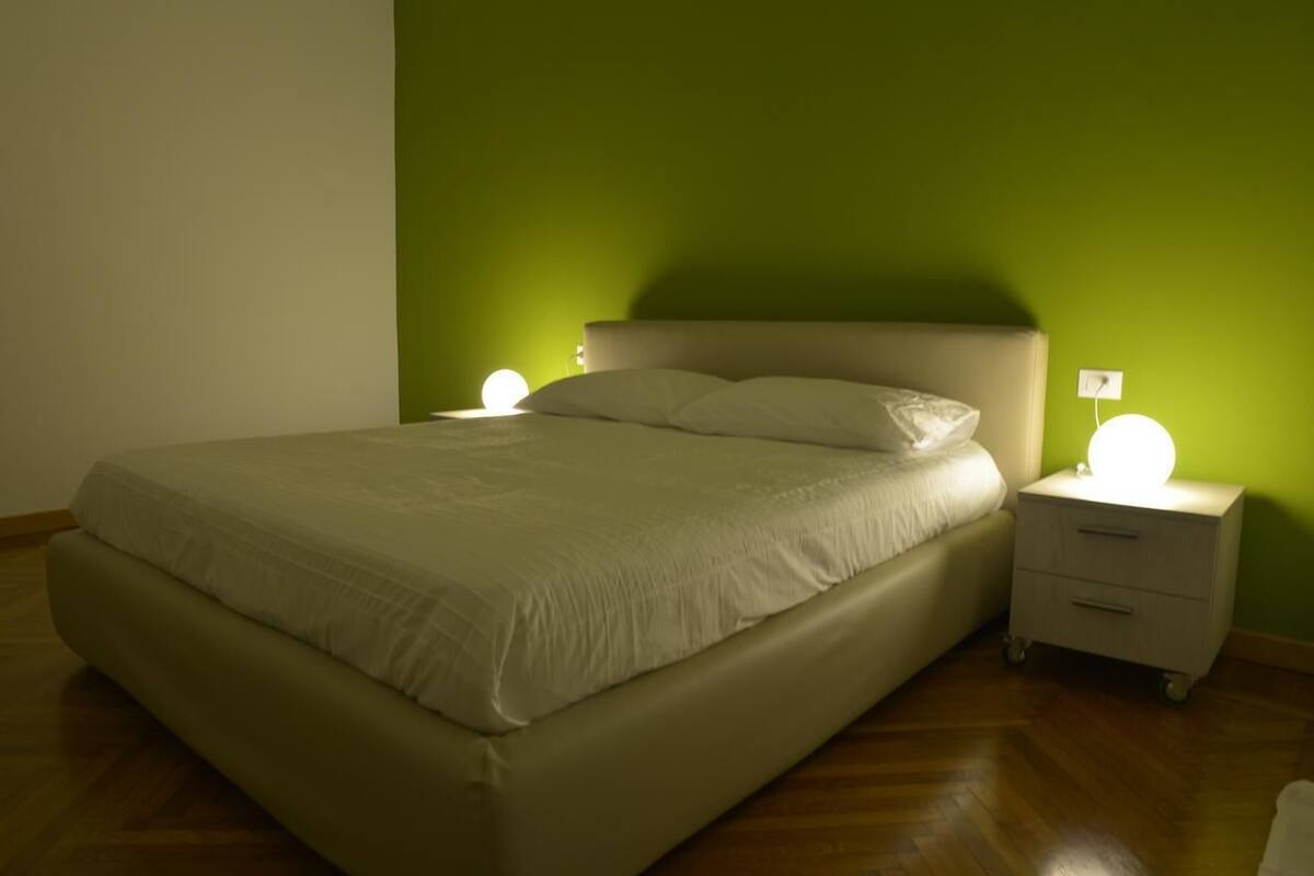 A neatly made bed with a headboard, two bedside tables with lamps, and a green wall.