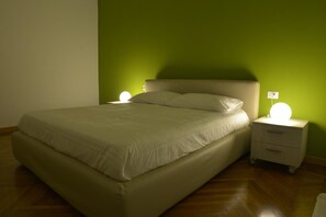 A neatly made bed with a headboard, two bedside tables with lamps, and a green wall.