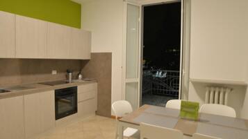 Une cuisine moderne avec un coin repas, une porte-fenêtre coulissante donnant sur un balcon et une vue sur le paysage urbain nocturne.