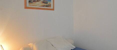 A bedroom with a bed, pillows, a bedside table with a lamp, and a framed picture on the wall.