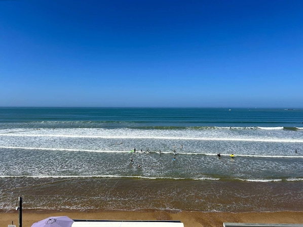 En strand med bølger, klar himmel og sandet kystlinje.