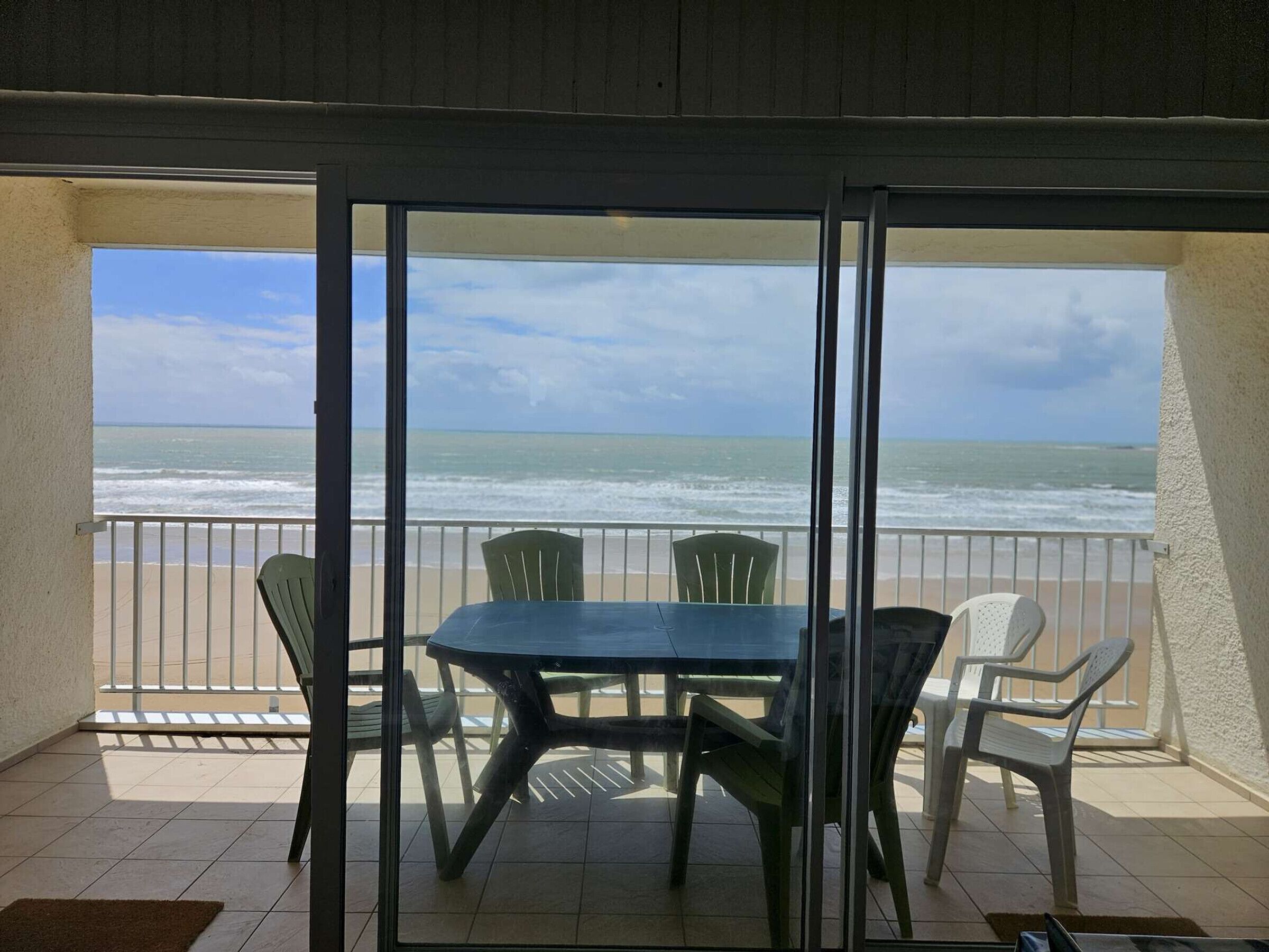 Un balcón con mesa y sillas, con vista a una playa y al océano.