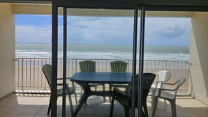 Un balcon avec une table et des chaises, donnant sur une plage et l’océan.
