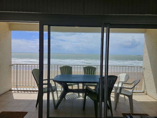 A balcony with a table and chairs, overlooking a beach and ocean.