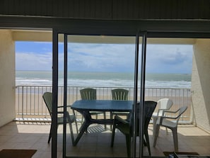 En balkon med bord og stole, med udsigt over en strand og hav.