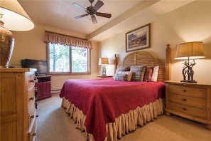 A bedroom with a bed, a ceiling fan, a window, a dresser, and a lamp.