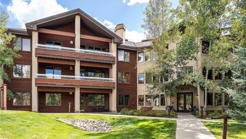 A multi-story building with a prominent balcony on the second floor, a stone pathway leading to the entrance, and a well-maintained lawn.