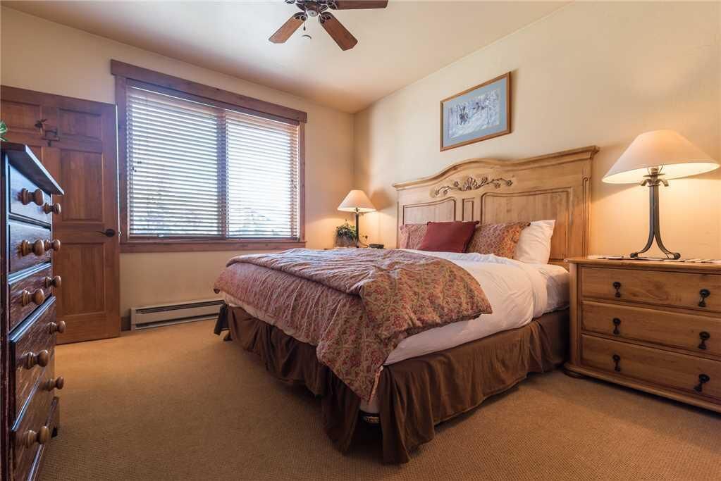Ein Schlafzimmer mit einem hölzernen Bett, zwei Nachttischlampen, einem Deckenventilator, einem Fenster mit Jalousien und einem Schminktisch.