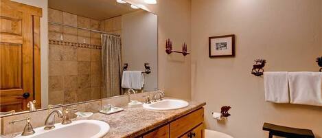 A bathroom with two sinks, a toilet, a shower, and a vanity with a mirror.