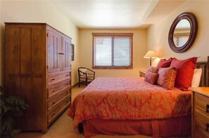 A bedroom with a large bed, a dresser, a chair, a window with blinds, and a mirror on the wall. - 3308 Champagne Lodge, Trappeur's Crossing Apartment 3 (Steamboat Springs)