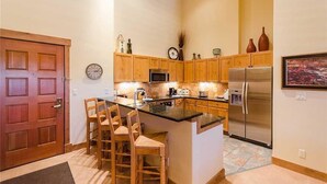 A kitchen with wooden cabinets, a stainless steel refrigerator, a microwave, and a clock on the wall. - 3308 Champagne Lodge, Trappeur's Crossing Apartment 3 (Steamboat Springs)