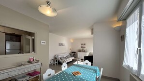 Een compacte kamer met een eettafel, een kitchenette, een bed en een raam met gordijnen.