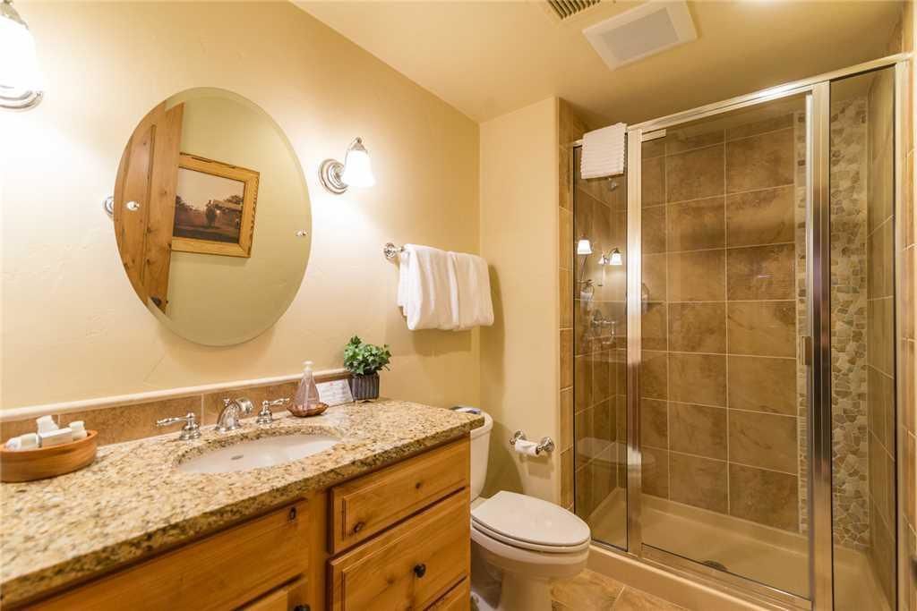 A bathroom with a granite countertop sink, wooden vanity, a round mirror, a toilet, and a glass-enclosed shower.