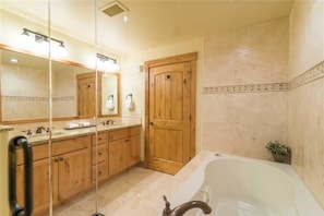 A bathroom with a large mirror, wooden cabinets, a bathtub, and a potted plant.