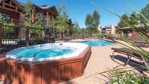 A hot tub and a pool area with lounge chairs and a wooden deck. - 5101 Emerald Lodge, Trappeur's Crossing Apartment 3 (Steamboat Springs)