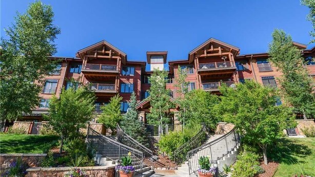A multi-story building with balconies, a central staircase, and surrounding greenery.