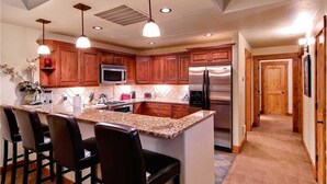 A modern kitchen with wooden cabinets, a granite countertop, stainless steel appliances, and pendant lighting.