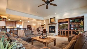 A spacious living room with a fireplace, comfortable seating, and a kitchen in the background. - 5106 Emerald Lodge, Trappeur's Crossing Apartment 5 (Steamboat Springs)