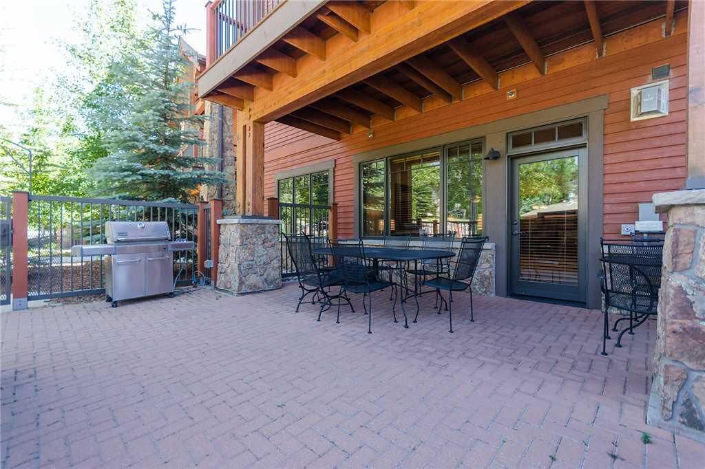 An outdoor patio with a grill, stone pillars, and metal chairs.