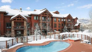 A large building with a pool area, surrounded by snow-covered trees and a clear sky. - 5109 Emerald Lodge, Trappeur's Crossing Apartment 4 (Steamboat Springs)