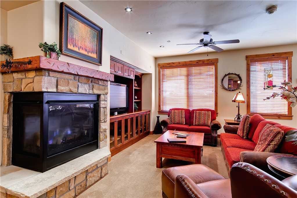 A living room with a stone fireplace, a television, a red sofa, and a ceiling fan.