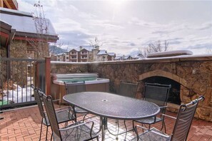 A patio with a stone wall, a hot tub, and a fireplace. - 5111 Emerald Lodge, Trappeur's Crossing Apartment 2 (Steamboat Springs)