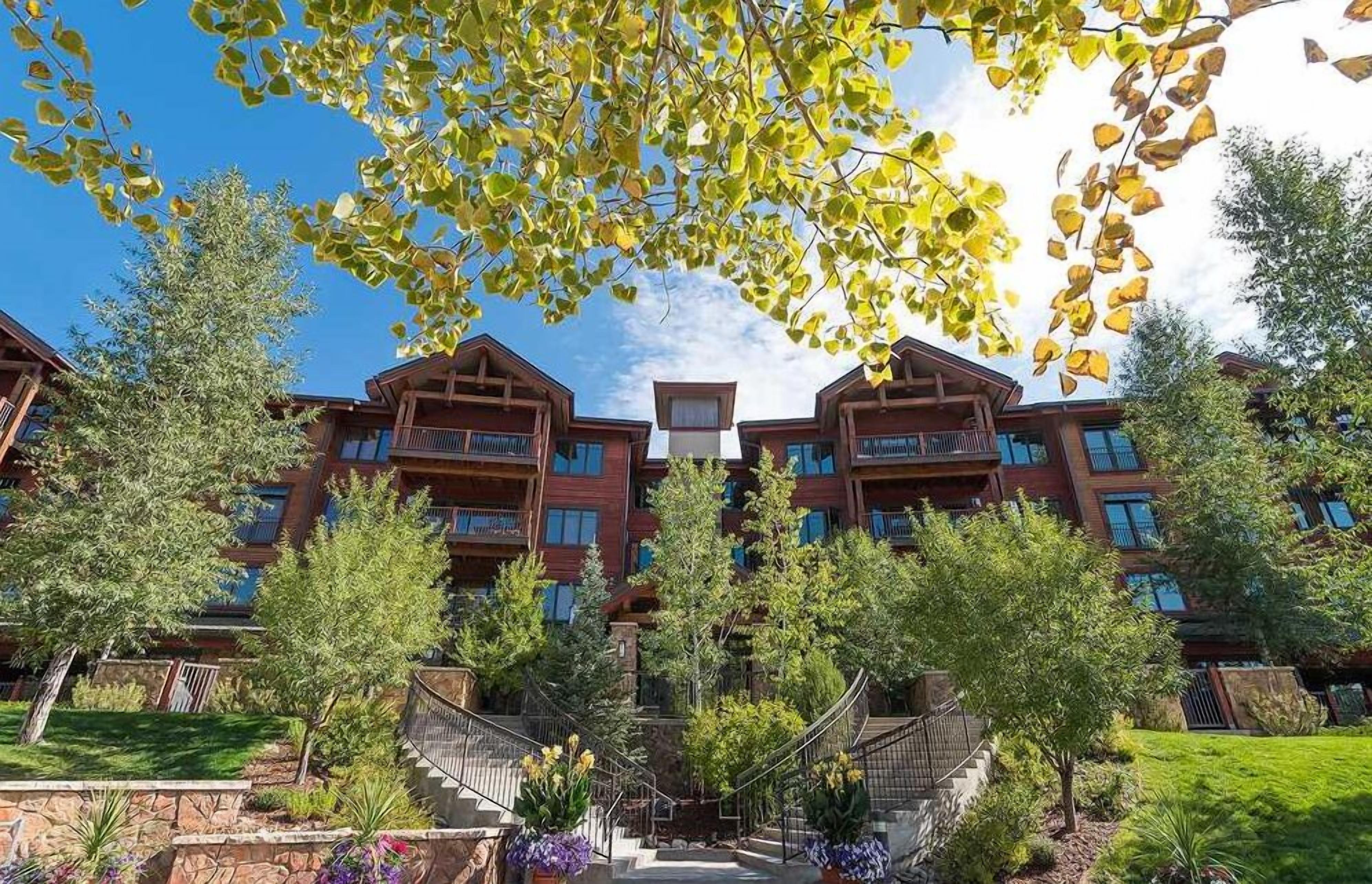 A multi-story hotel with a central staircase, surrounded by lush greenery and trees.