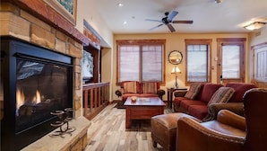 Un salon chaleureux avec une cheminée, des fauteuils confortables et un ventilateur de plafond.