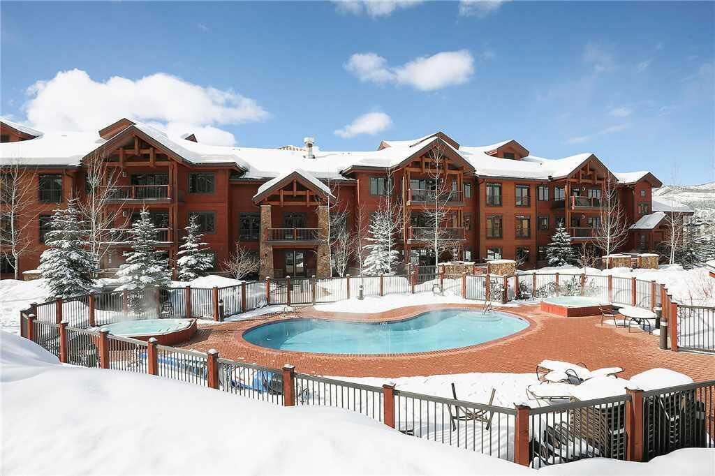 Uma grande pousada com piscina, cercada por neve, com várias varandas e um espaço de lazer em tijolos.
