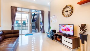 A modern living room with a leather sofa, a flat-screen TV, a wooden entertainment unit, and a large window with curtains. - Baan Chom Chan Pool Villa (Hua Hin)