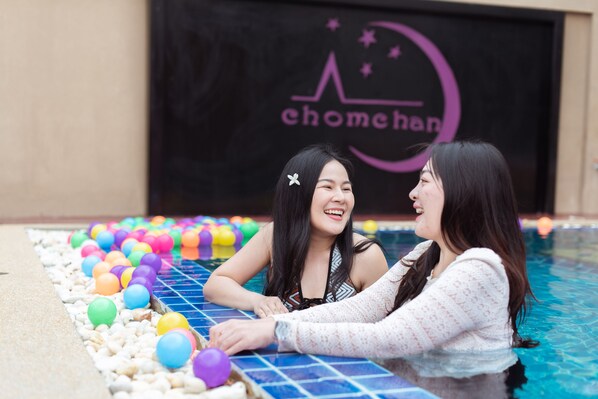 Two people in a swimming pool with colorful balls and a black wall with a logo.